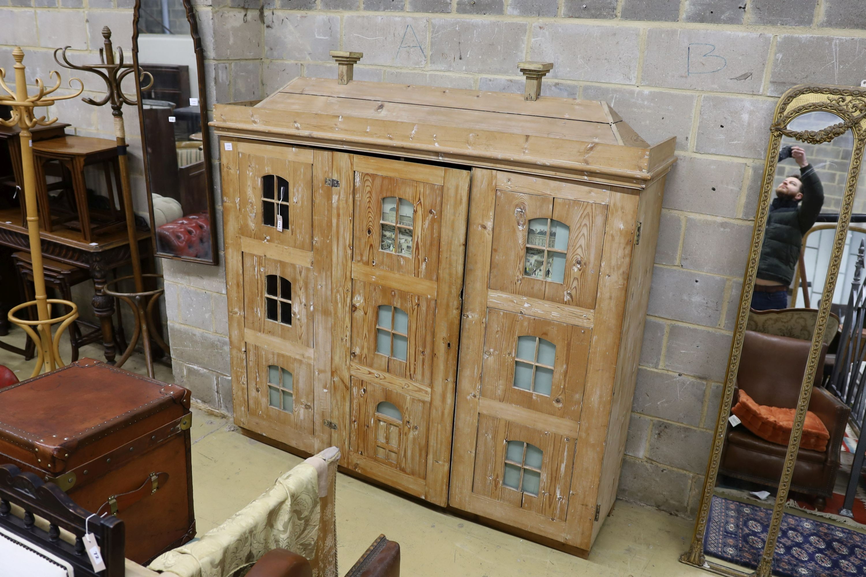 A 19th century stripped pine hall cupboard modelled as a dolls house the two door nine window facade enclosing a compartmented interior, width 182cm, depth 46cm, height 192cm